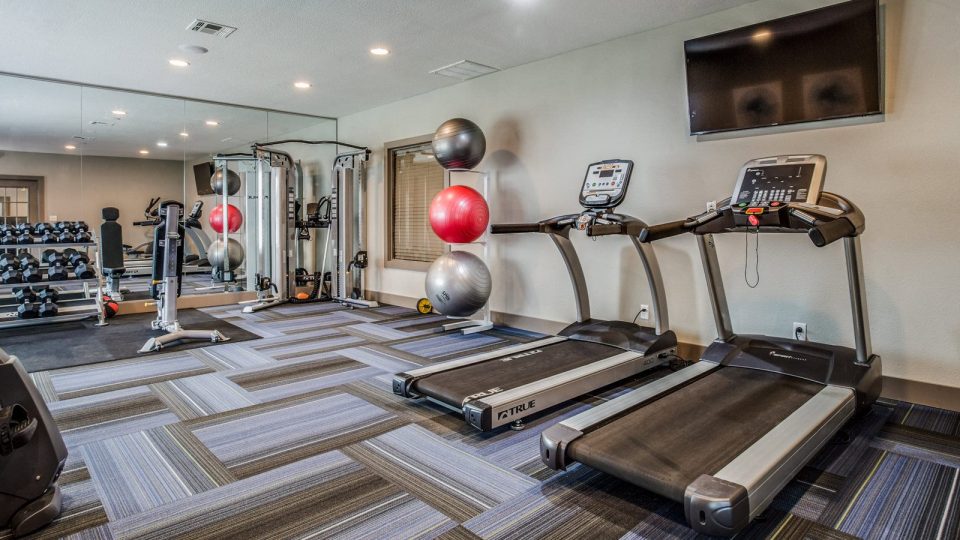 a gym room with treadmills, exercise machines and televisions at The Mark at 2600