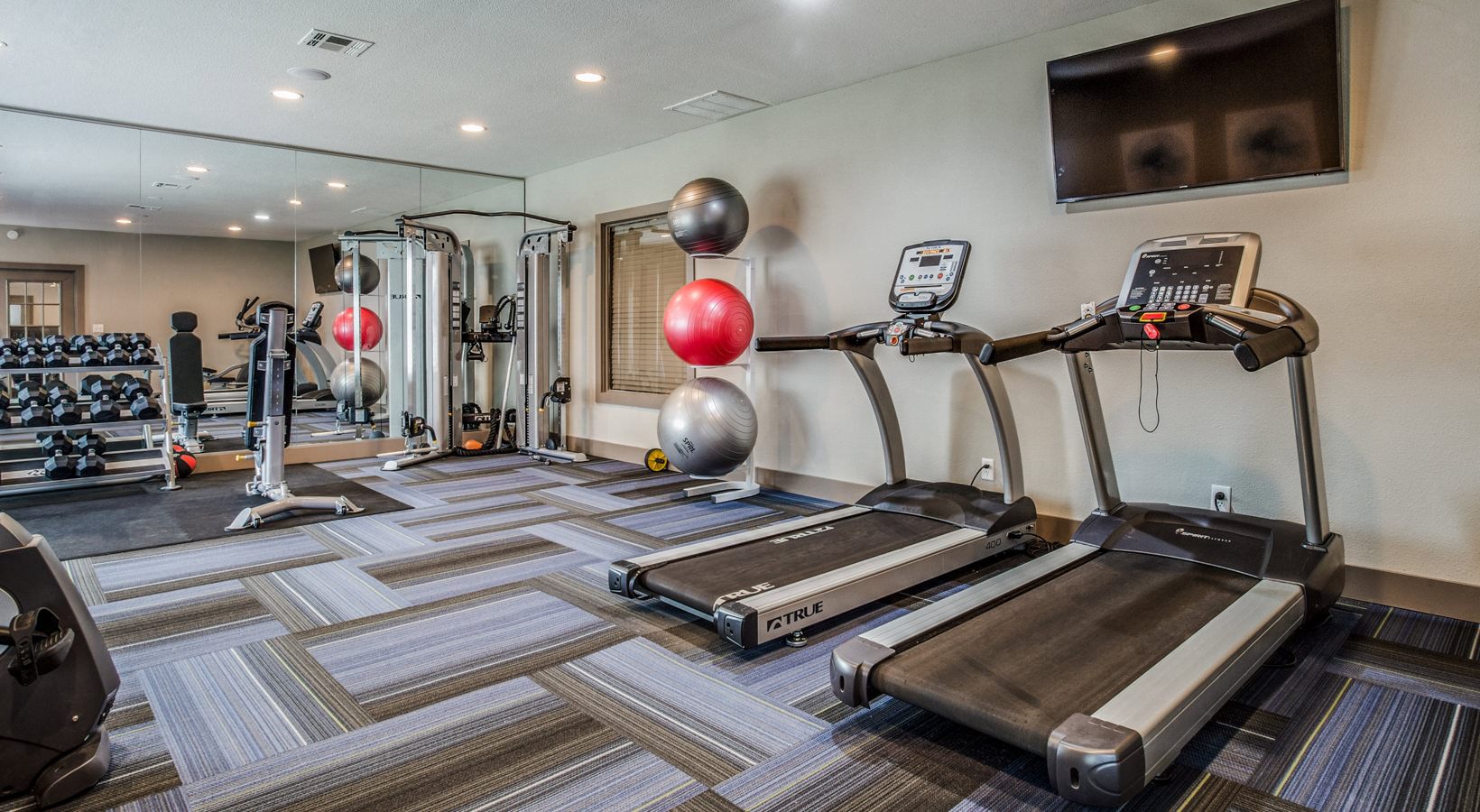 a gym room with treadmills, exercise machines and televisions at The Mark at 2600
